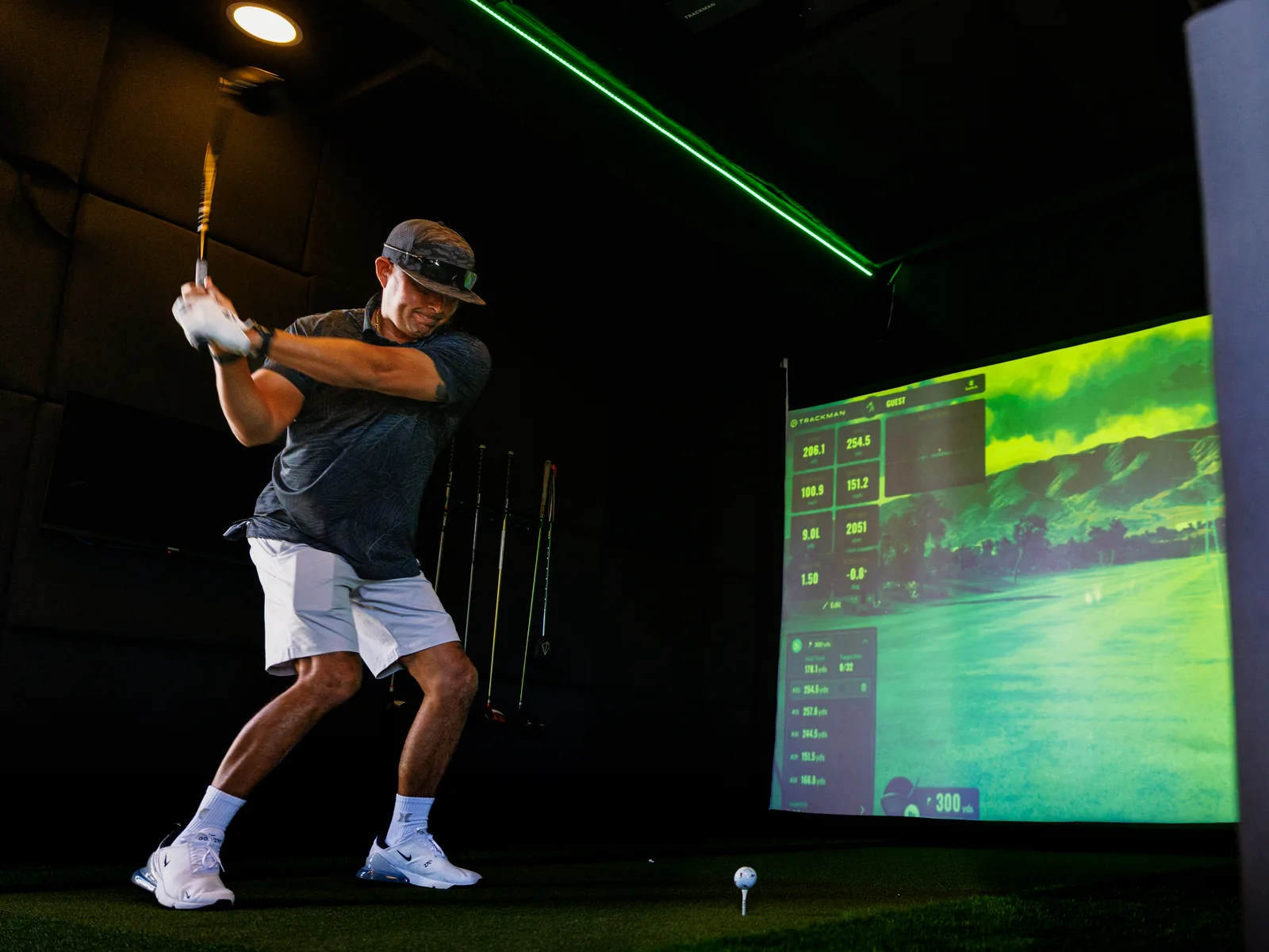 A guest at the top of the backswing inside the trailer with live TrackMan shot numbers on the screen beside him
