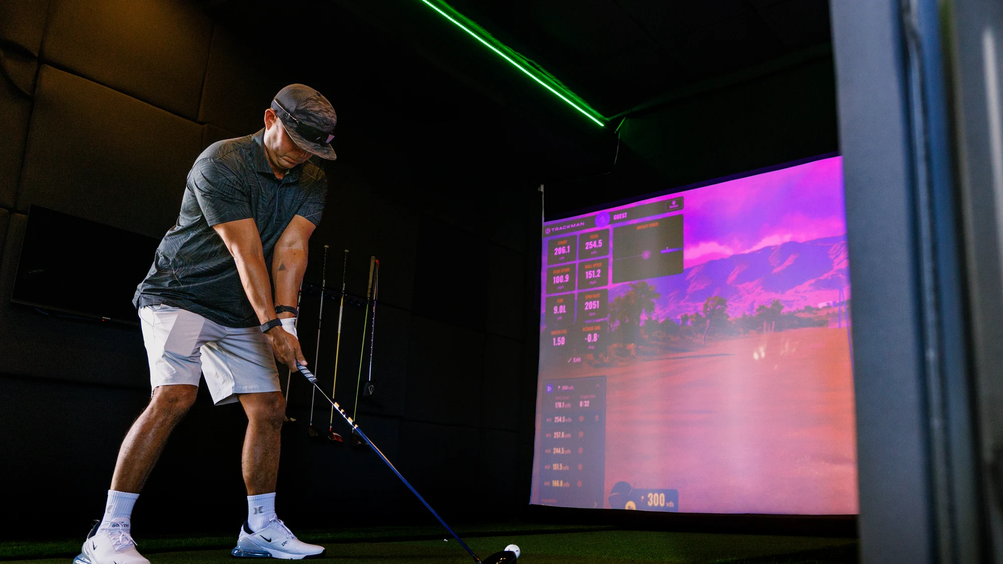A golfer set up over the ball with a driver inside the SwingLab trailer, the TrackMan screen lit ahead of him