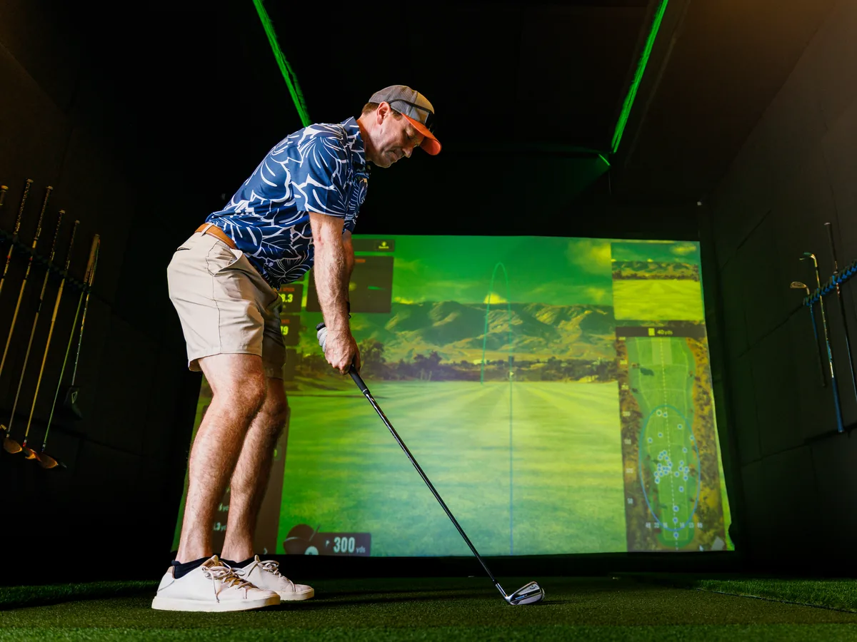 A golfer set up over the ball inside the trailer, the TrackMan course view filling the screen in front of him
