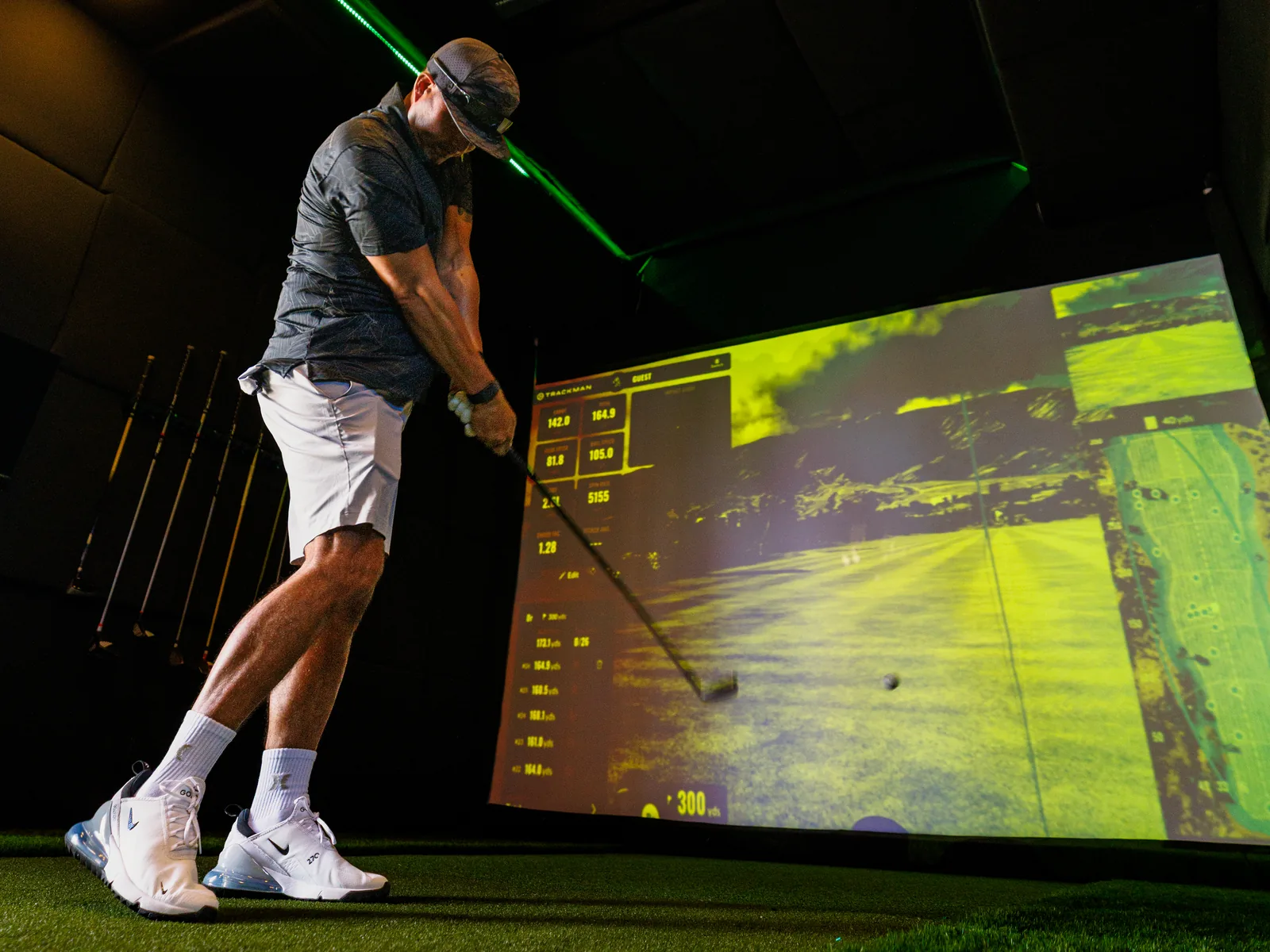 The full interior bay of the SwingLab trailer at an Oahu event, a golfer swinging on the turf beside the lit TrackMan screen