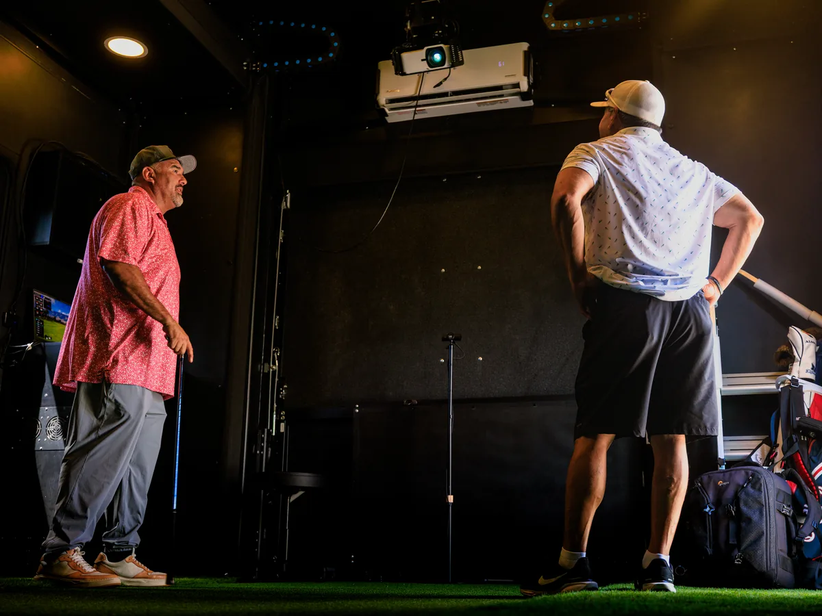 Daren Kawika Martin talking a guest through the setup inside the SwingLab trailer, simulator screen lit behind them