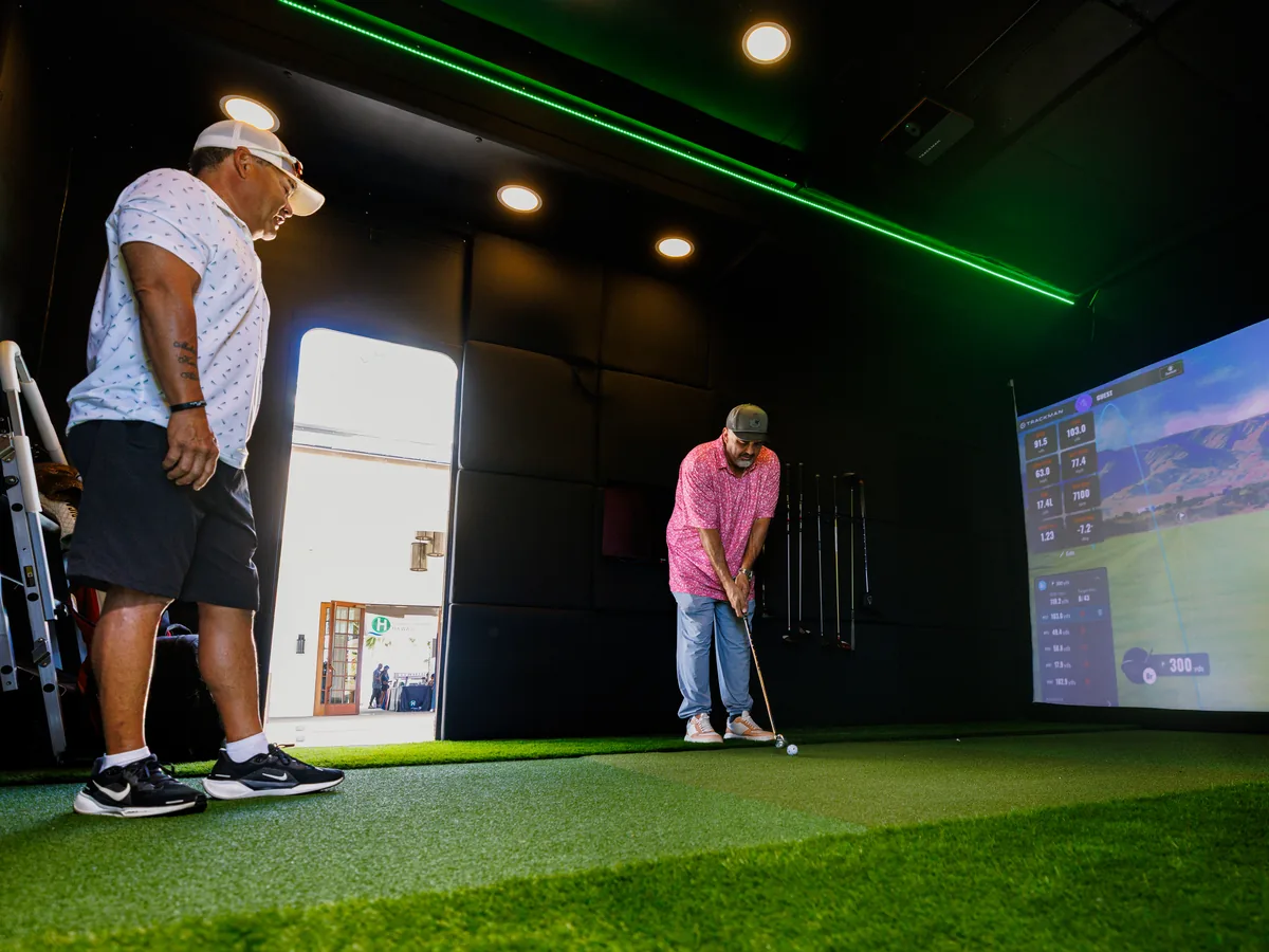 One guest lining up a shot on the trailer turf while a second watches from beside the open door
