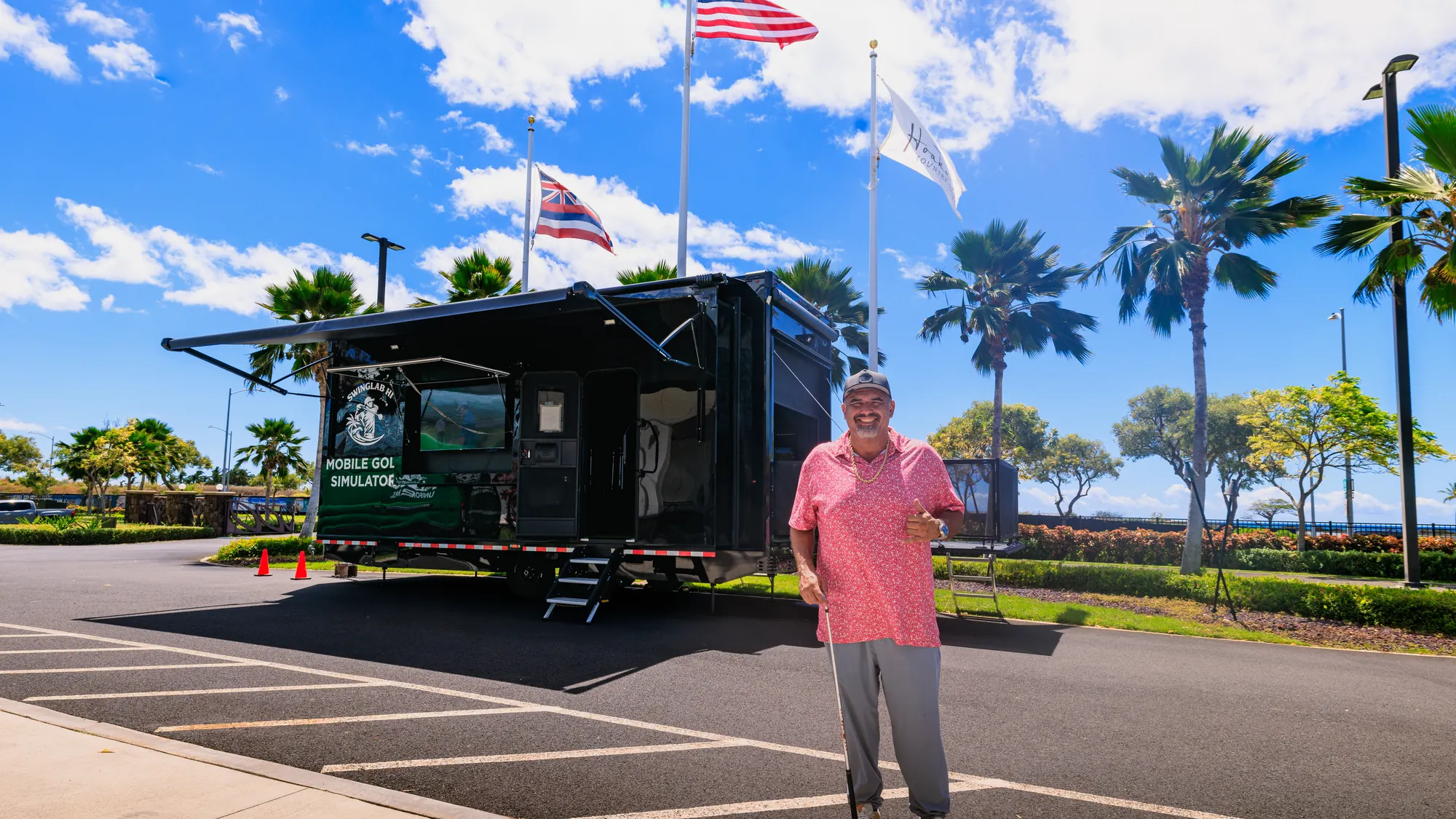 The SwingLab Hawaii mobile golf simulator trailer set up and open for play at a club on Oahu, awnings out under the flags