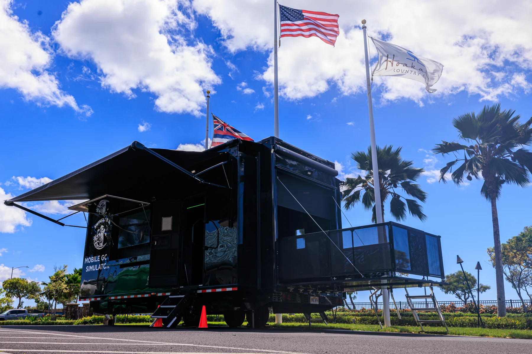 The SwingLab Hawaii mobile golf simulator trailer parked at a club on Oahu, awning extended under the US and Hawaii flags