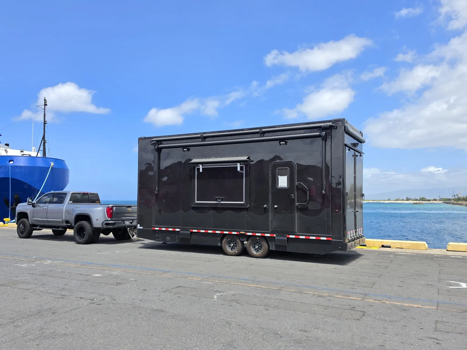 The SwingLab Hawaii mobile golf simulator trailer hitched to a pickup on the waterfront, on its way to an event on Oahu
